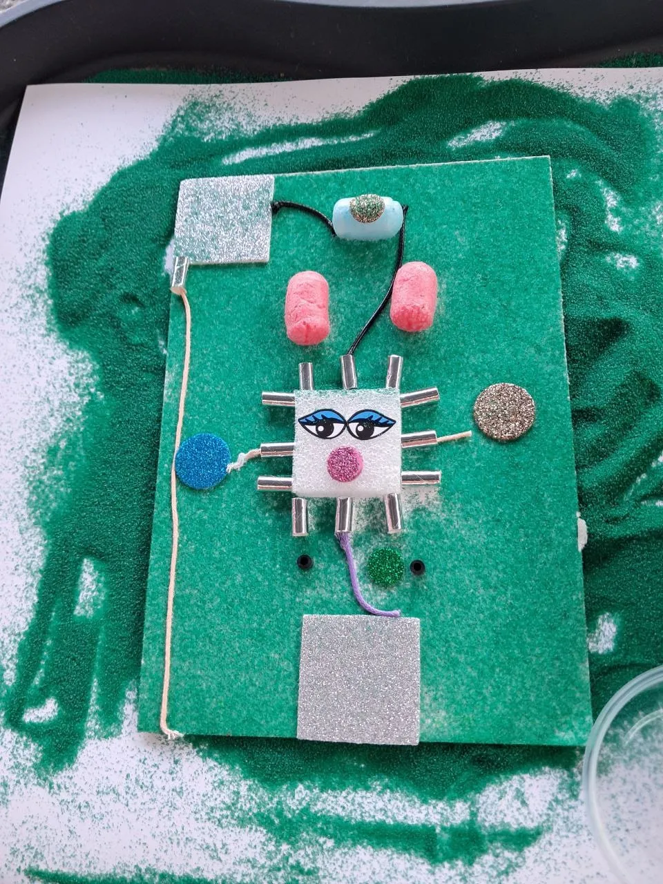 Sandbild mit einem Gesicht aus Knöpfen und Moosgummi