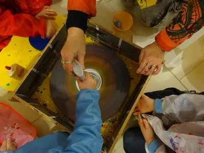 Kinderhände und eine Erwachsene gestalten gemeinsam ein Schleuderbild mit Farbe